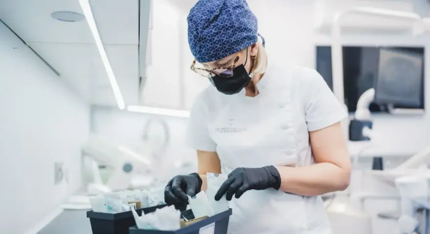Dentystka w czepku i masce przygotowuje materiały, w tym te do zabiegów z użyciem abrazji powietrznej.