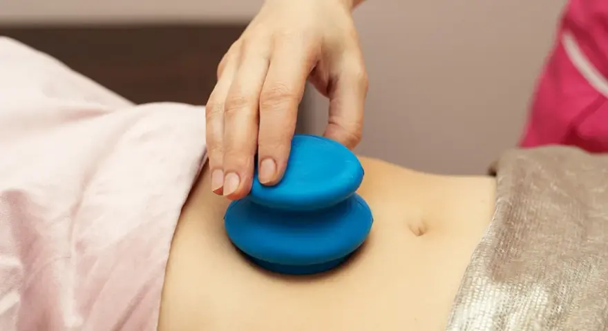 Dłoń terapeuty wykonuje masaż banką chińską na brzuchu pacjentki.