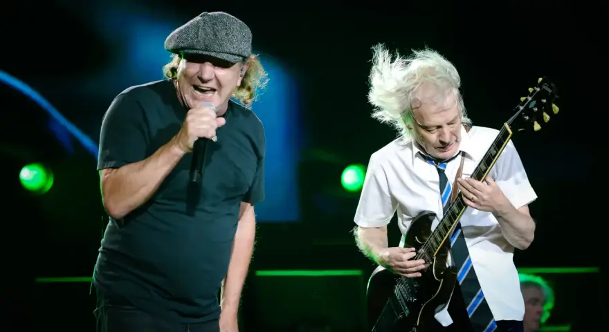 Brian Johnson śpiewa, Angus Young gra na gitarze podczas jednego z legendarnych **AC/DC koncertów**.