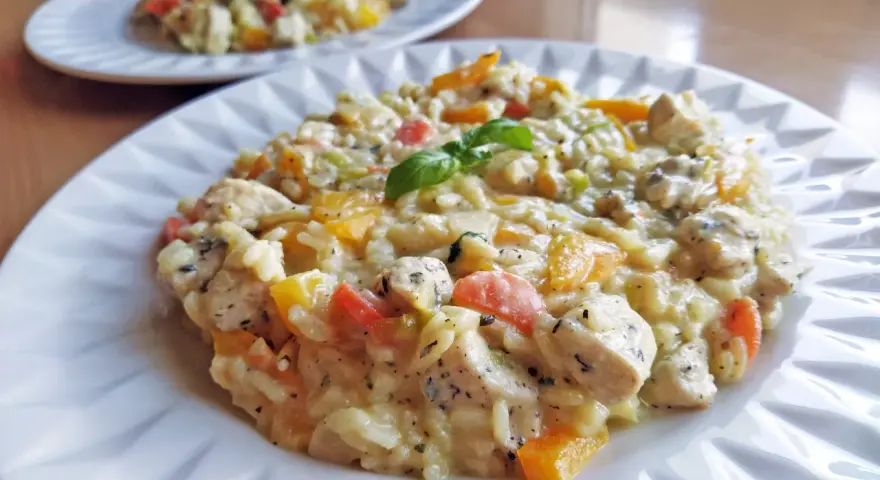 Szybkie risotto z warzywami i kurczakiem, udekorowane listkiem bazylii. Pyszne i kolorowe danie na talerzu.
