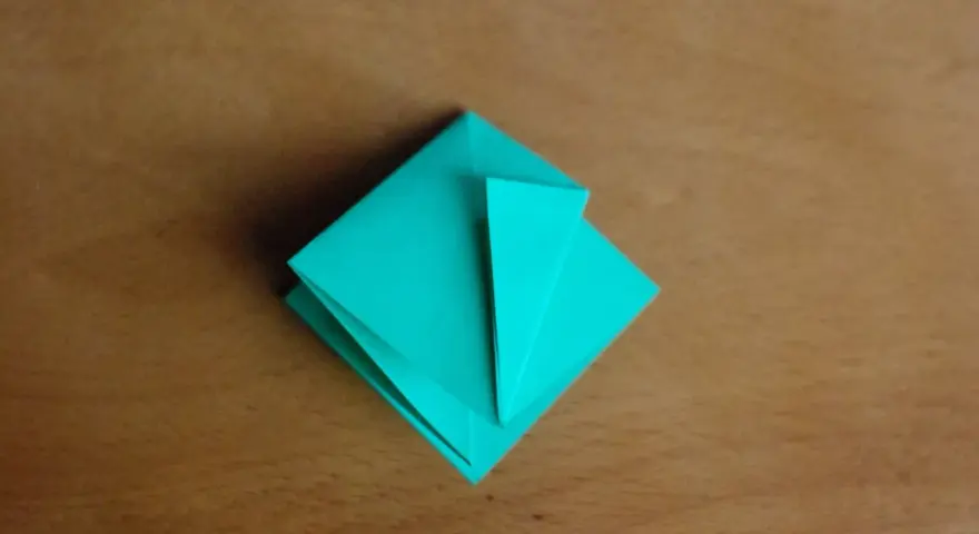 Krok 15 instrukcji, jak zrobić kwadrat z papieru. Turkusowa origami na drewnianym tle.