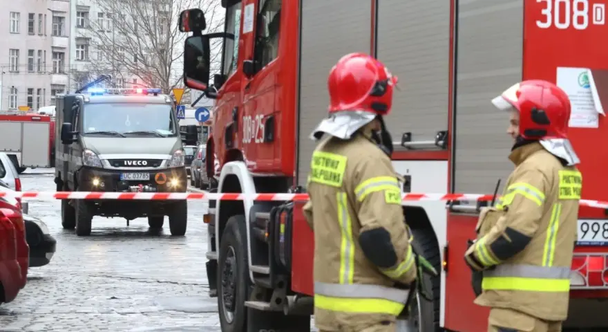 Dwóch strażaków w hełmach i mundurach stoi przy wozie strażackim. W tle wóz saperski. Starszy ogniomistrz zarobki to marzenie wielu, ale oni służą.