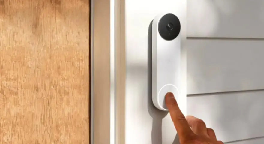 Un dedo presiona qué es el timbre inteligente, un dispositivo blanco con cámara negra, junto a una puerta de madera.
