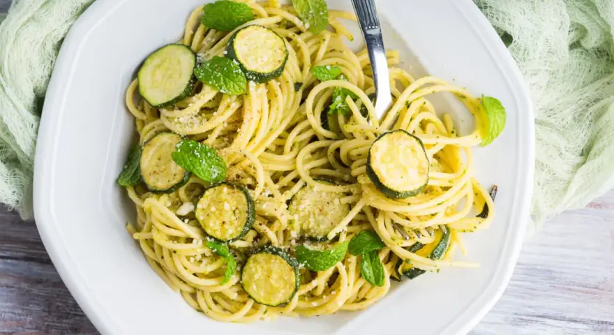 Spaghetti con zucchine cremosa, guarniti con foglie di menta fresca e parmigiano grattugiato. Un piatto leggero e gustoso.