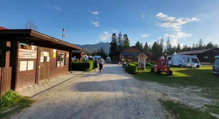 Słoneczny dzień na **camping Oravice**. Drewniany budynek recepcji, przyczepy kempingowe i zielone wzgórza w tle.