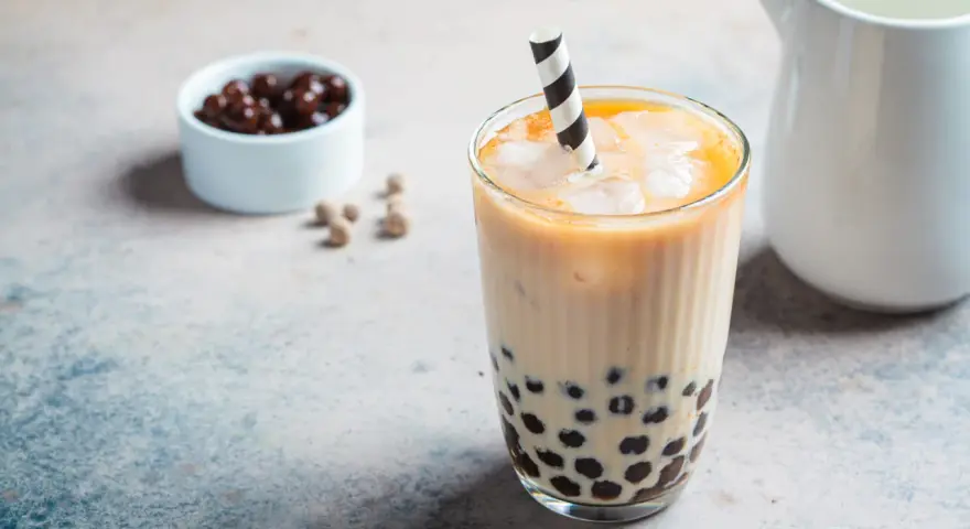 Erfrischendes Bubble Eis mit Tapiokaperlen und Eiswürfeln in einem Glas, daneben eine Schale mit dunklen Perlen.