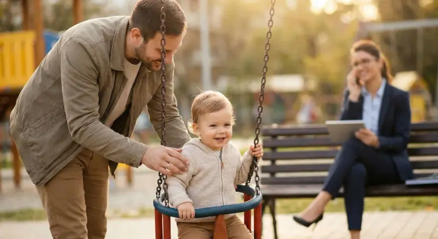 Ein Vater schaukelt sein Kind. Im Hintergrund telefoniert eine Frau. Die Frage, an welchen Kosten sich der Vater beteiligen muss, bleibt offen.