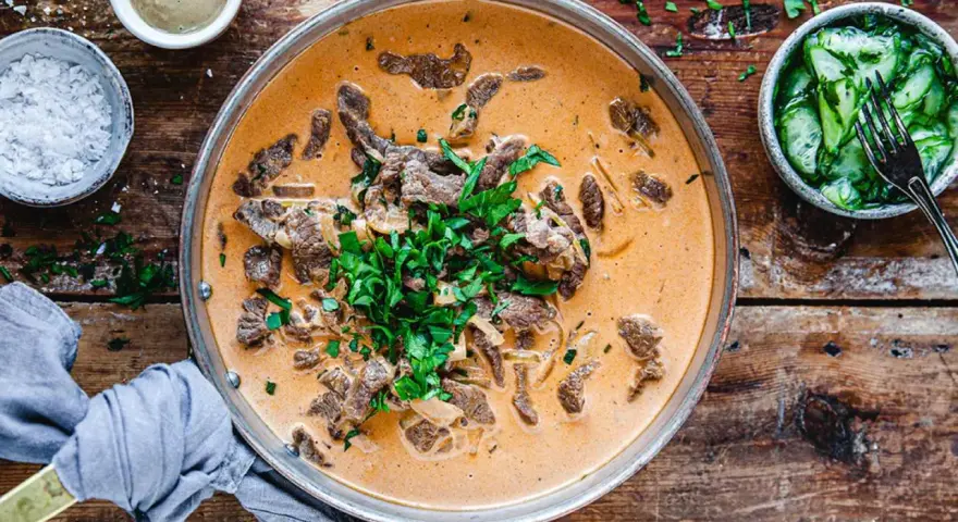 En krämig biff stroganoff med färsk persilja, serverad med gurksallad och en liten skål med senap. Perfekt vin till biff stroganoff.