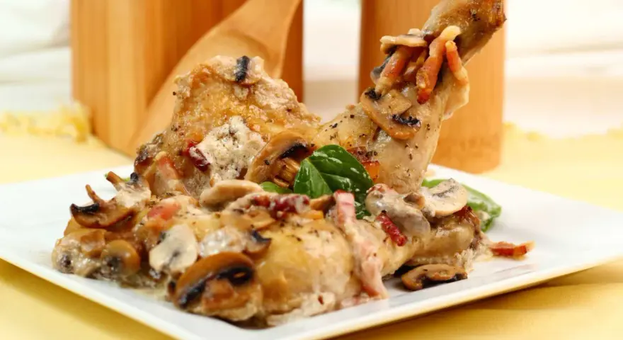 Delicioso pollo con champiñones y tocino en una cremosa salsa, servido en un plato blanco.