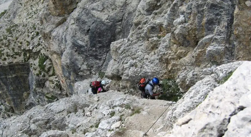 Dwóch turystów pokonuje via ferraty w Dolomitach, wspierając się na stalowej linie.
