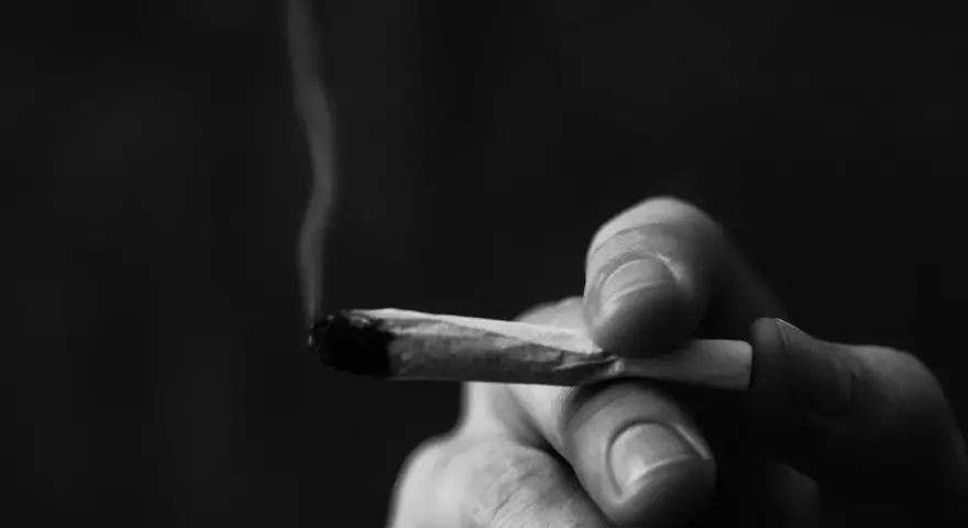 A hand holds a lit joint, smoke curling upwards. This image prompts reflection on whether Christians can smoke weed.