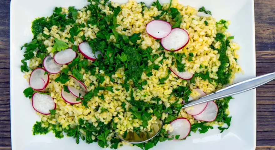 En fräsch bulgursallad med rädisor och färska örter, serverad på en vit tallrik med en sked.