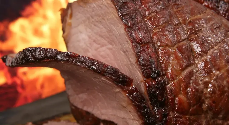 Un enchaud de porc juteux, rôti à la perfection, avec une croûte caramélisée et des flammes dans l'arrière-plan.