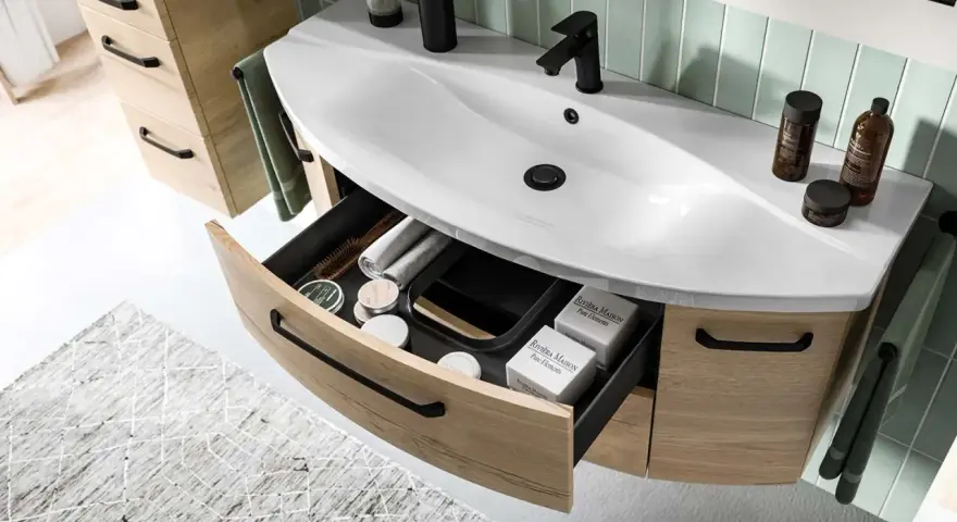 Aménagement salle de bain moderne avec lavabo blanc, robinetterie noire et tiroirs en bois clair organisés.