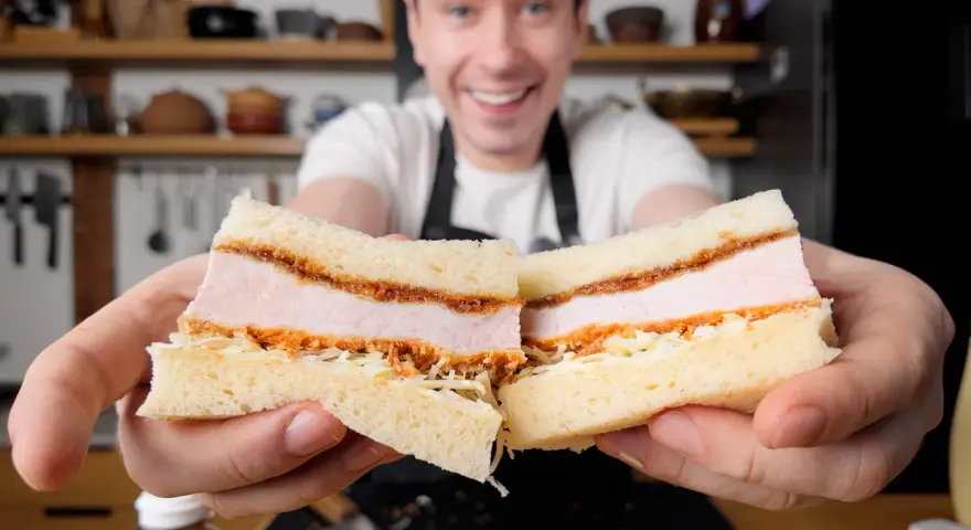 Uśmiechnięty mężczyzna prezentuje pyszne katsu sando z soczystym kotletem schabowym w panierce, delikatną kapustą i puszystym chlebem.