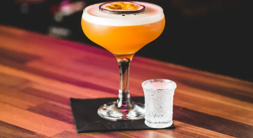 Pomarańczowy koktajl Pornstar Martini z owocem marakui, obok kieliszek z bąbelkami. Zastanawiasz się nad jego kcal?