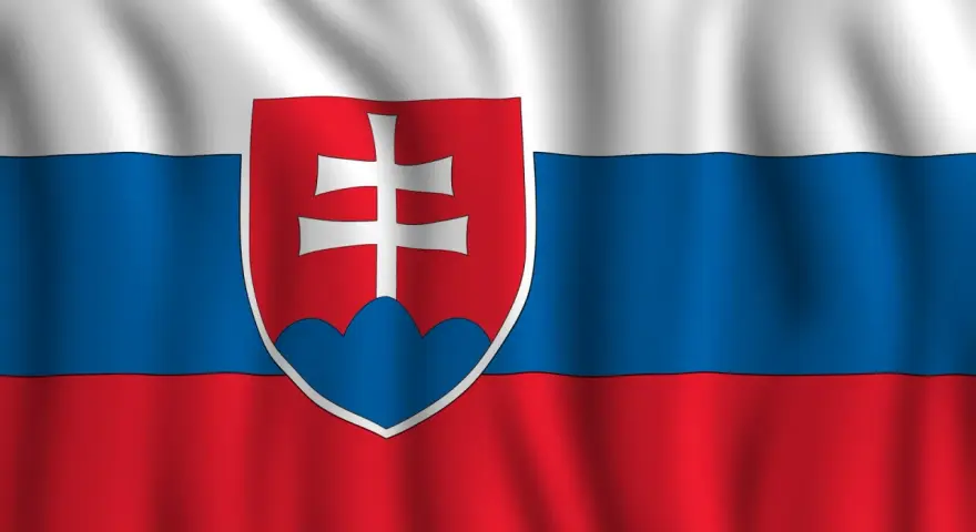 Flaga Słowacji powiewa na wietrze. Biało-niebiesko-czerwone pasy z godłem Słowacji po lewej stronie.