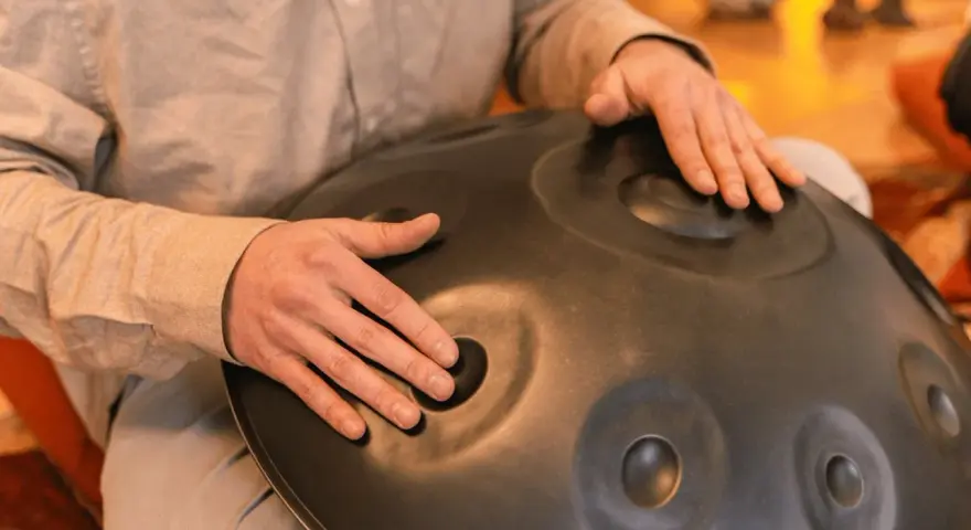 Dłonie grają na instrumencie typu hang drum, tworząc kojące dźwięki.