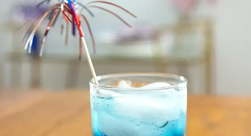 Niebieski drink z lodem i parasolką, przypominający letni koktajl z blue curacao.