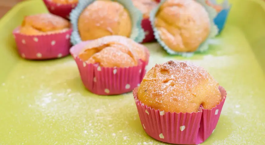 Leckere Muffins ohne Ei, bestäubt mit Puderzucker, in bunten Papierförmchen auf einer hellgrünen Platte.