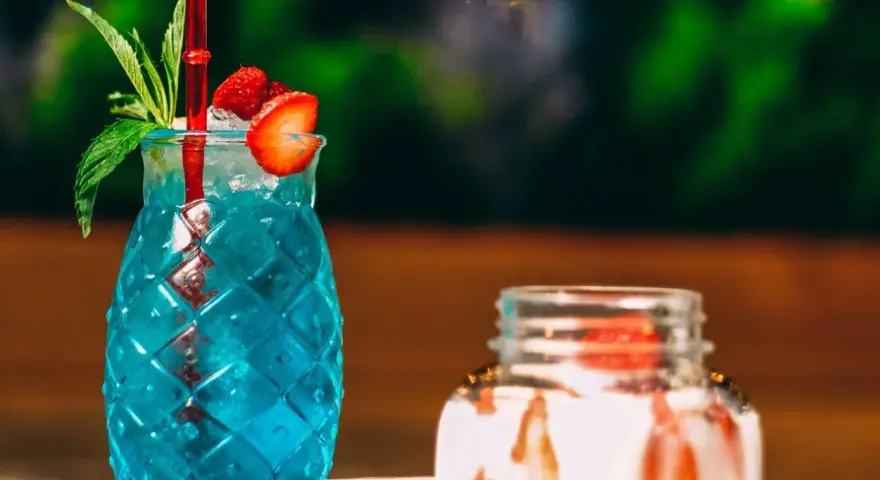 Orzeźwiający, niebieski drink z palemką, ozdobiony truskawką i miętą. Idealny na letnie popołudnie.