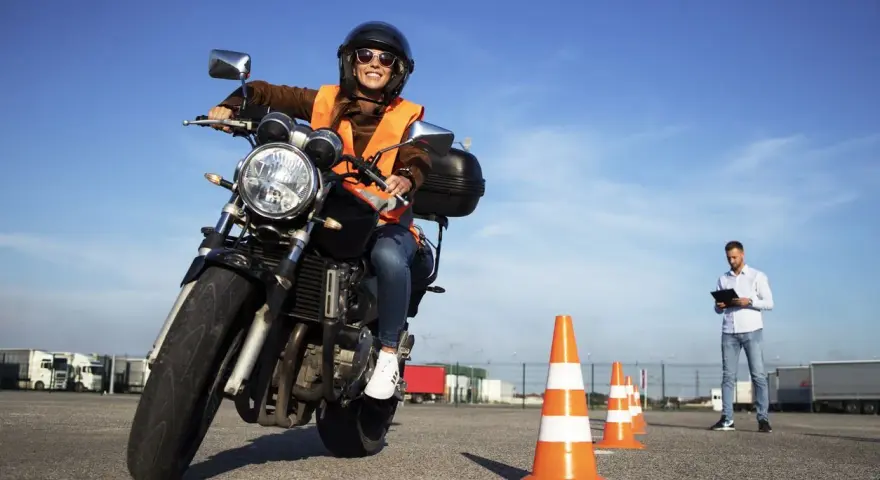 Joven sonriente en moto, lista para obtener el carnet de moto 49cc. Instructor observa en el fondo.