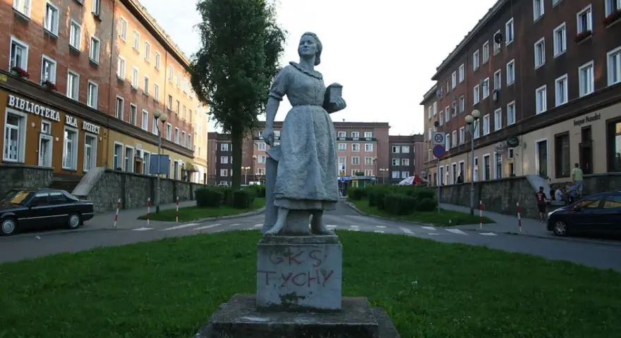 Pomnik w stylu socrealizmu na tle bloków mieszkalnych.