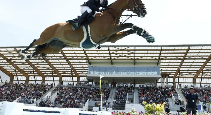 Un cavalier et son cheval s'envolent au-dessus d'une rivière lors d'un CSI Equitation. Le public applaudit dans les gradins.