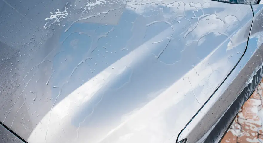 Krople wody i piany na masce srebrnego auta. Czy po woskowaniu płukać auto? Tak, aby uzyskać idealny połysk.