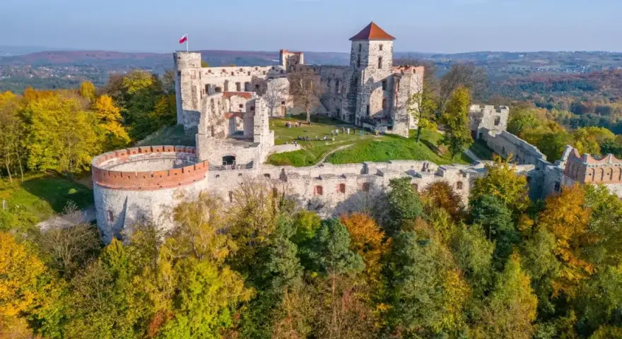 Ruiny zamku na Szlaku Orlich Gniazd, otoczone jesiennym lasem. Majestatyczne mury i wieże górują nad okolicą.