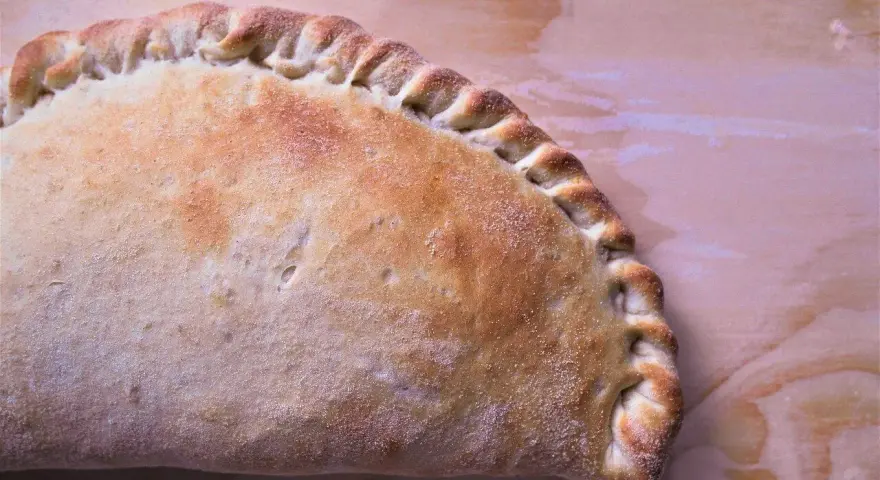Złocisty calzone, pieczony na drewnianym tle, z charakterystycznym, zaplecionym brzegiem. Idealny na szybki posiłek.