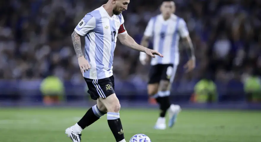Lionel Messi w koszulce Argentyny prowadzi piłkę, gotowy do zdobycia kolejnych bramek. Fani zastanawiają się, ile goli ma Messi.