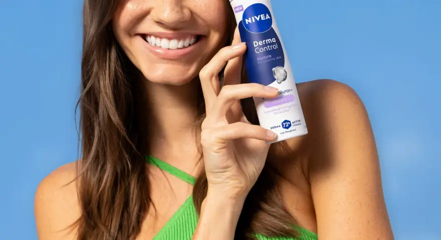 Uśmiechnięta kobieta trzymająca dezodorant Nivea Derma Control na tle niebieskiego tła.