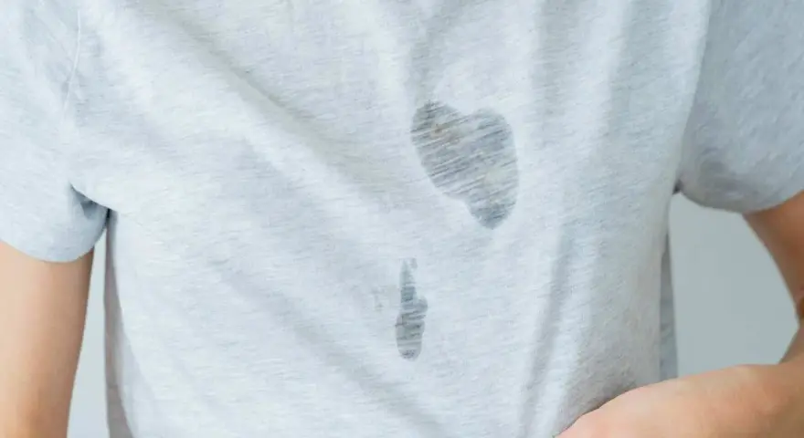 Gros plan sur une tache d'huile sur un vêtement gris clair. La tache est sombre et semble avoir pénétré le tissu.