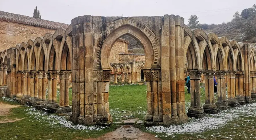 Ruinas de un claustro con arcos de piedra, evocando el nacimiento del Duero. Nieve ligera cubre el césped.