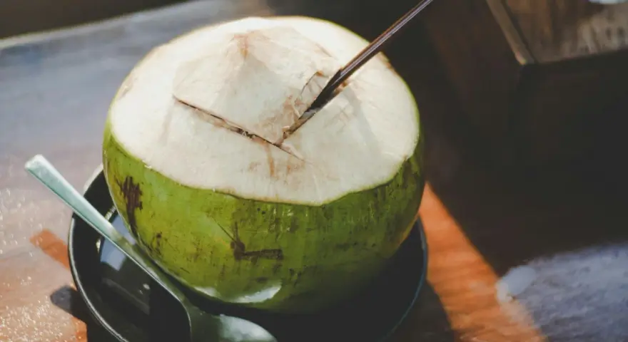 Une noix de coco verte ouverte avec une paille, prête à déguster. Découvrez les nombreux bienfaits de l'eau de coco pour une hydratation naturelle.