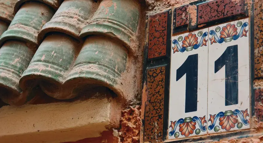 Numerologiczna 11 mężczyzna, jak liczba 11 na ozdobnej tabliczce obok zielonych dachówek, symbolizuje intuicję i duchowość.