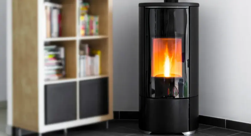 Stufa a pellet moderna in camera da letto, con fiamme vive che illuminano l'ambiente. Accanto, una libreria in legno con libri.