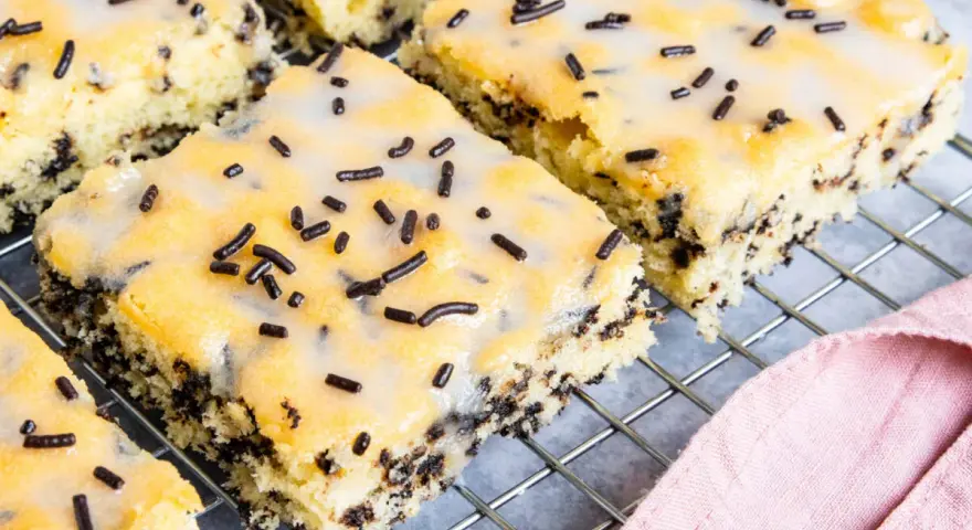 Saftiger Ameisenkuchen vom Blech, mit Zuckerguss und Schokostreuseln verziert, auf einem Kuchengitter.
