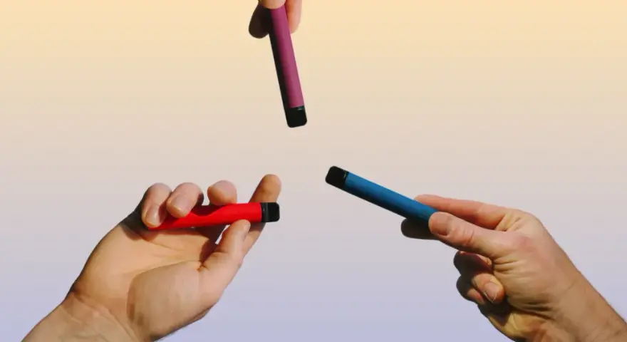 Manos sostienen vapers de colores: rojo, azul y morado. Una opción para un vaper sano.
