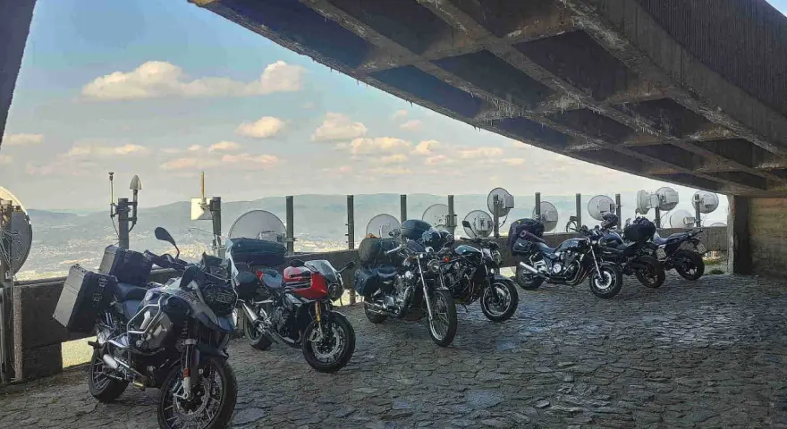 Motocykle pod betonowym zadaszeniem, z widokiem na krajobraz przypominający szwajcarskie Czechy.