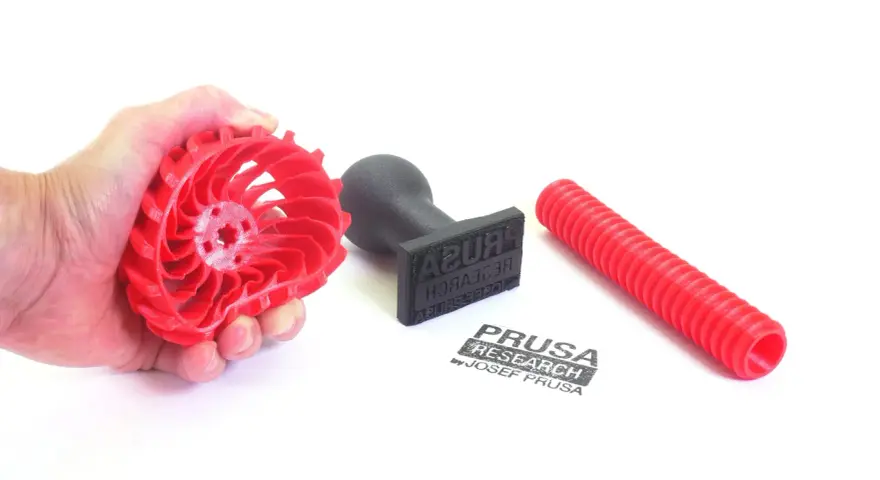 Czerwony, elastyczny filament w kształcie wirnika, stempel z logo Prusa Research i czerwona rurka.