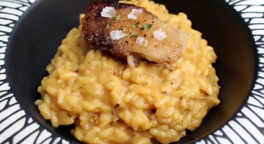 Cremoso risotto a la milanesa, coronado con un trozo crujiente y salpicado de sal marina y hierbas.