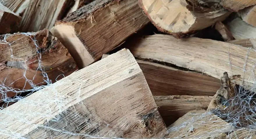 Gros tas de bois humide, prêt pour le poêle. Les bûches sont emballées dans un filet blanc.