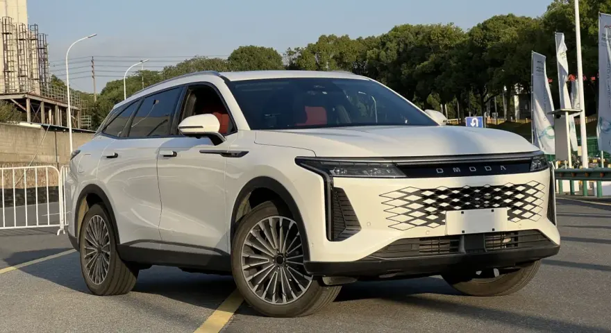 Biały OMODA 9 Super Hybrid z czerwonym wnętrzem na tle przemysłowego krajobrazu.