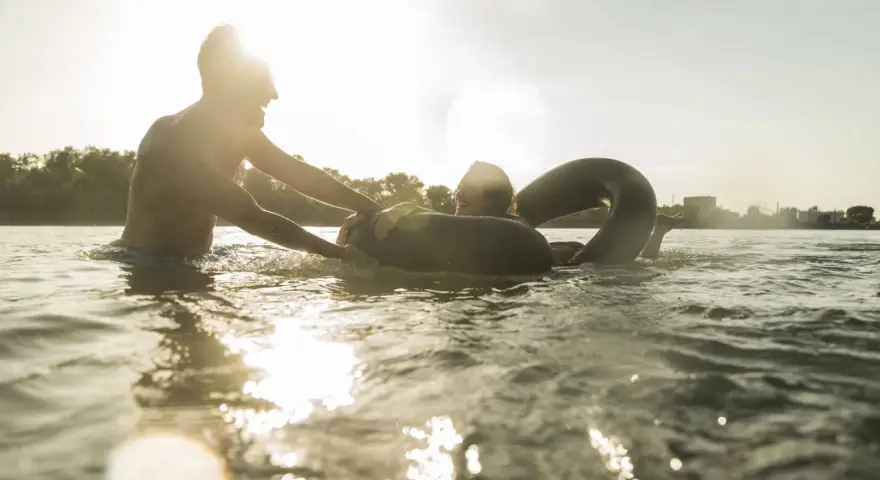 Ein Mann hilft einer Frau mit einem Schwimmring im Wasser. Ein sonniger Tag am Badesee Braunschweig.