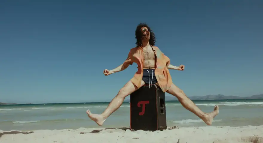 Mężczyzna na plaży skacze na głośniku, słuchając stare piosenki na lato.