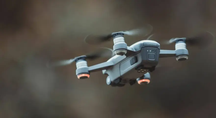 A drone hovers mid-air, its propellers a blur. Red anti-collision lights glow on its arms, ensuring safe flight.