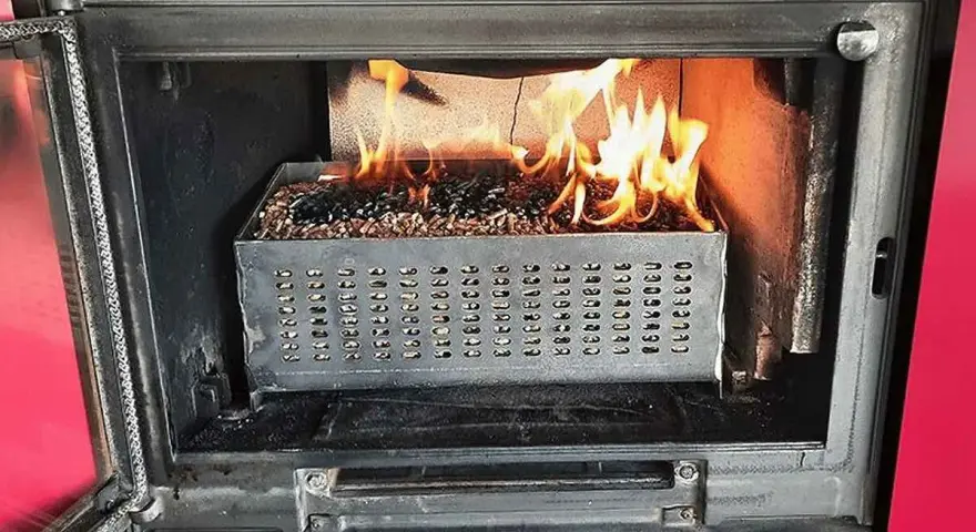 Estufa de pellets ardiendo dentro de un hueco de chimenea. El combustible se quema en una bandeja metálica perforada.
