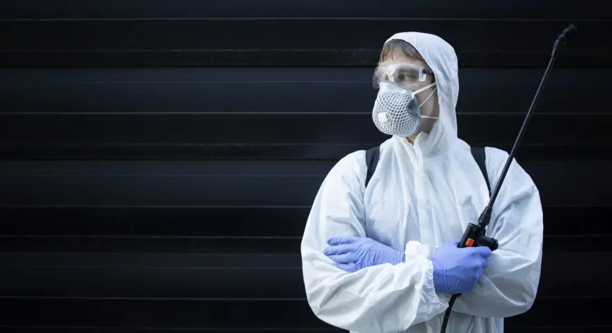 Persona con traje protector, mascarilla y gafas, sosteniendo un pulverizador. ¿Cuánto tiempo esperar después de fumigar?